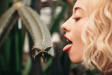 Beauty portrait of brutal blonde woman with red lips in tropical forest and lick barbed cactusの写真素材
