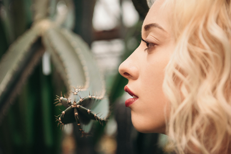 Beauty portrait of blonde woman with red lips in tropical forest looking on cactusの写真素材
