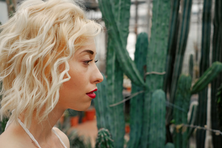 Beauty portrait of blonde woman with red lips in tropical forest looking on cactusの写真素材