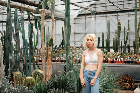 Fashionable portrait of beautiful young woman with blonde hair standing in the succulent cactus garden in beautiful tropical greenhouseの写真素材