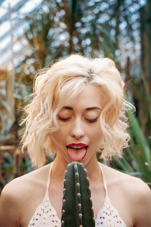Funny portrait of blond woman tropical botanical garden holding barbed cactus in the hands and try to lick itの写真素材