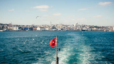 Turkish national flag fluttering on Bosphorus from ship with beautiful city view on background at sunny day, Istanbul, Turkeyの写真素材