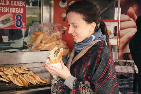 Young woman travel in Turkey and taste traditional turkish street food from fried fish, vegetables and breadの写真素材