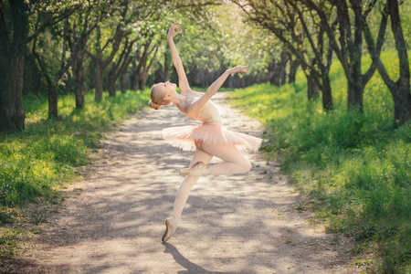 Young woman with perfect body in white tutu dancing in the green landscape. Beautiful ballerina showing classic ballet poses. Concept of female tenderness and freedomの写真素材