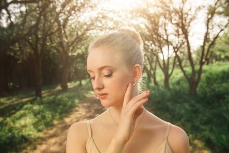 Portrait of beautiful ballerina in the green landscape. Romantic and tender feeling of young dancer girl in white tutu in floral garden at sunsetの写真素材