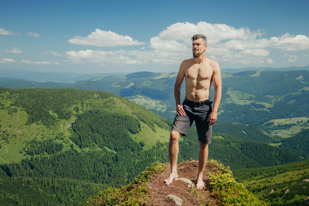 Young naked athletic man standing on the mountain rock and looking at landscapeの写真素材
