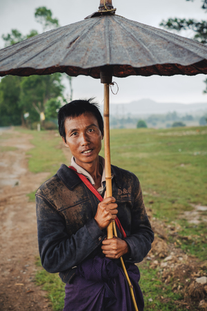 Kalaw, Myanmar - May 22, 2016: Portrait of burmese man in traditional clothes and handmade umbrella in Kalawのeditorial素材