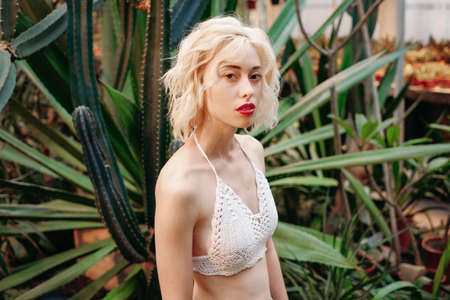 Fashion portrait of blond hair woman and perfect figure posing in the floral spring summer garden in the tropical greenhouse. Glamour lady in green palm leaf.の写真素材