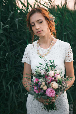 Woman in white wedding dress holding beautiful bouquet on green wall backgroundの写真素材