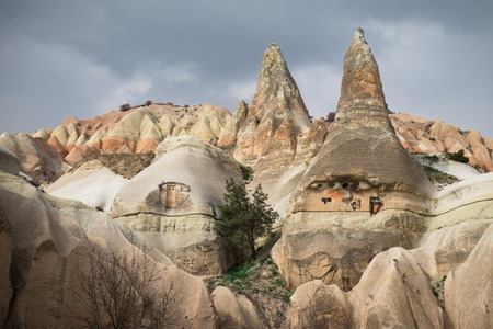 Colorful valley with cave houses and fairy chimneys rock formation with cloudy sky in rural Cappadocia landscape near Goreme village, Turkeyの写真素材
