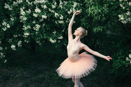 Young woman in white tutu dancing in the green flowers landscape. Beautiful ballerina showing classic ballet poses and jumping high into the air. Concept of female tenderness and harmony life.の写真素材