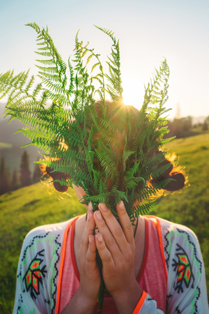 Atmospheric woman portrait with face covered by green fern leaves at sunset. Feel freedom and enjoying the nature conceptの写真素材