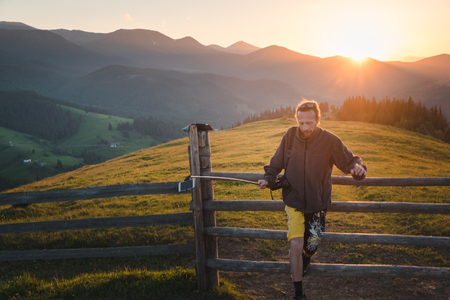 Hipster man jump over the fence  holding wood selfie stick with mobile at sunsetの写真素材
