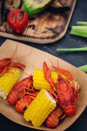 Red boiled crayfish serving with grilled vegetables and greenery on dark wooden table, Top viewの写真素材