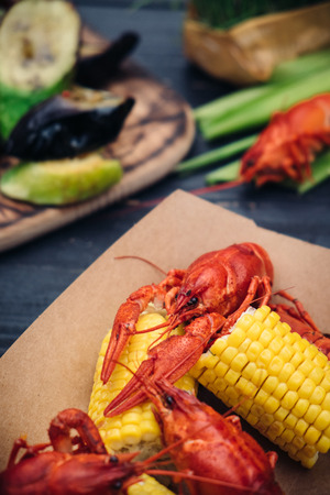Red boiled crayfish serving with grilled vegetables and greenery on dark wooden table, Top viewの写真素材