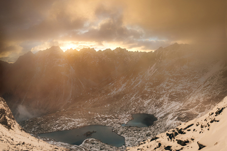 Beautiful mountain lake in High Tatras National Park  with snow covered mountains in clouds at gold sunset. Slovakiaの写真素材