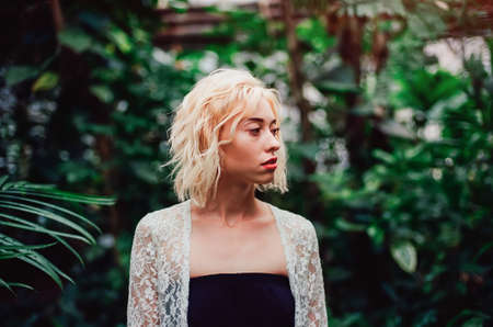 Fashion portrait of beautiful young with blonde hair and perfect figure posing in the palm leaves in the jungle. Scanned film with grainの写真素材