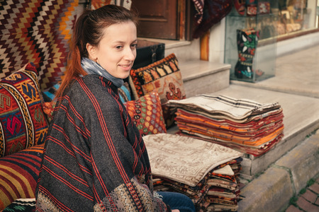 Traditional Turkish souvenir fabric market on the street and a beautiful traveler sitting on the pavement smilingの写真素材