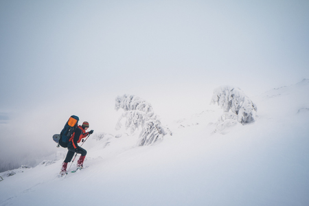 Man hiking on snow hills with trekking sticks and snowshoes over the clouds. Winter sport activity. View from the back sideの写真素材