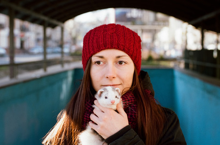 Cute girl in red hat holding white ferret in the hand. Beautiful portrait. Friendship between people and animal. Scanned film with grainの写真素材