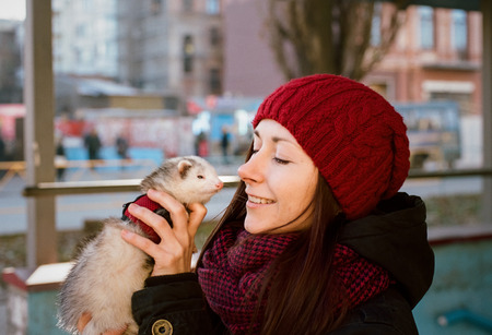 Cute girl in red hat holding white ferret in the hand. Beautiful portrait. Friendship between people and animal. Scanned film with grainの写真素材