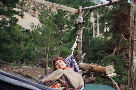 Tourist having rest in hammock on a fresh air, cuddling in her own poncho, smiling.の写真素材