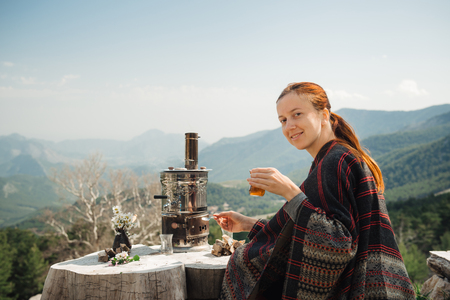 Smiling young traveler having a Turkish tea at the wooden table high in the mountains. Looking at camera.Closeupの写真素材