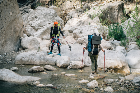 Friends traveling together crossing the mountain river by stepping on the rocks in Turkeyの写真素材