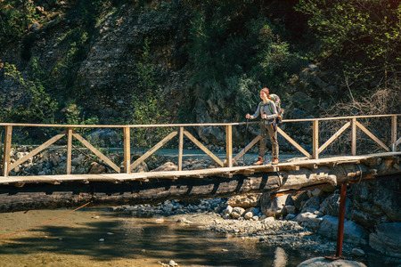 Happy female traveler crossing the wooden bridge over the mountain rivulet on a sunny dayの写真素材