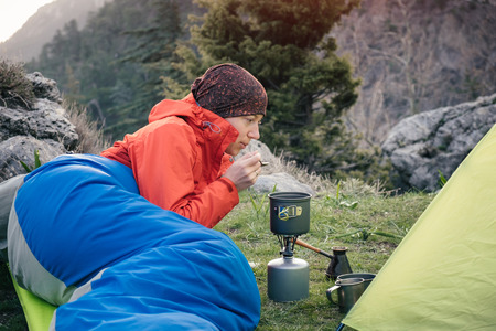 Tourist in a sleeping bag preparing food on the gas burner in the mountains in Turkeyの写真素材