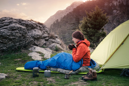 Traveler sitting on the ground next to the tent and drinking hot coffee, warming upの写真素材