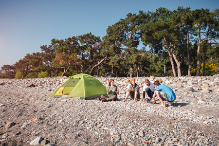 Friends traveling together sitting on a beach trying to cook dinner on a gas burner in Turkeyの写真素材