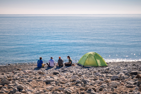 Friends traveling together (shot from back) sitting on a beach near the green tent bonding, relaxing. Turkeyの写真素材