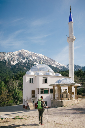 Silver dome mosque with a traveler standing in front of it on a background of Tahtali on a sunny dayの写真素材