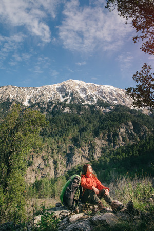 Traveler sitting on the ground next to her backpack taking sunbath on a background of Tahtali on a sunny dayの写真素材