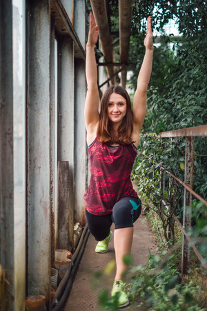 Young woman in a sporty clothes standing in warrior pose in the greenhouse passage.Looking at camera.の写真素材
