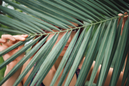 Portrait of young woman on background of palm leaf.Looking through leaves. の写真素材