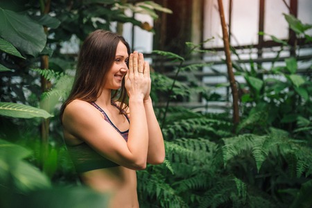 Closeup of happy smiling young woman meditating,doing namaste hand gesture at botanical garden. Healthy lifestyle concept.の写真素材