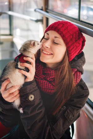Happy young woman having a moment with her cute ferret on a tram. Woman and a pet concept.の写真素材