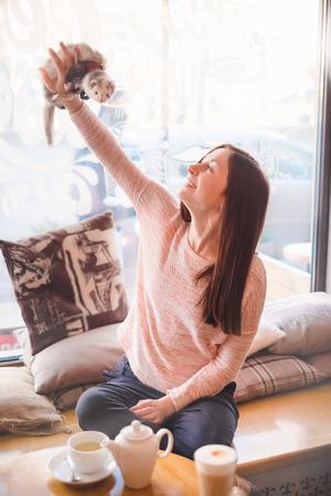Smiling girl fooling around with her pet ferret at a cafe window sill in the morning.Woman and a pet concept.の写真素材