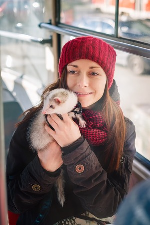 Young woman with her ferret exploring city on a tram on a sunny cold day. Woman and a pet concept.の写真素材