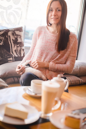 Beautiful girl with long brown hair having a good time with her favorite pet ferret at a cafe window sill. Woman and a pet concept.の写真素材