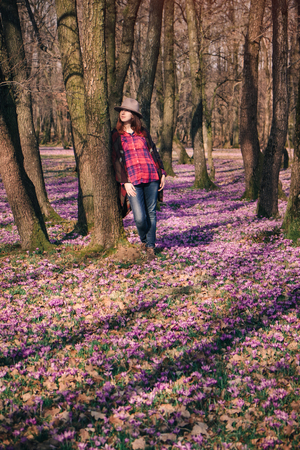 Sensual young lady with the sun in her red hair, standing among blooming nature, enjoying aroma of purple crocuses in Spring. Inspiration and wanderlust travel concept.の写真素材