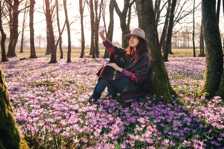Beautiful smiling traveler taking selfie in the blossoming forest in the morning. Inspiration and wanderlust travel concept.の写真素材