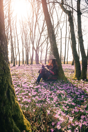 Beautiful girl with long hair in a hat and colorful poncho, matching purple flowers around, taking selfie of Spring forest on a sunny morning.Vertical orientation. Inspiration and travel concept.の写真素材
