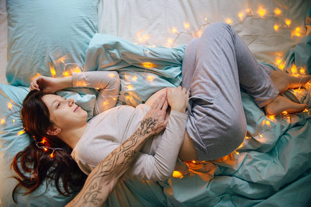 Young modern family expecting for a child. Husband embracing women belly in the bedの写真素材