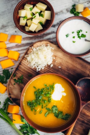 Tasty and healthy vegetarian food on wooden background. Top view of pumpkin cream soup served by yogurt, cheese and greeneryの写真素材