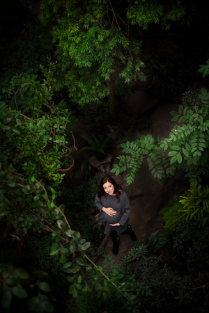 Full length portrait of beautiful pregnant redhead posing among trees, caressing her belly with hands.Looking at camera. Top view. Pregnancy and expecting concept.の写真素材