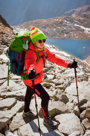 Full length portrait of blonde caucasian hiker in colorful outfit and sunglasses with walking sticks posing on top of mountain overlooking at Popradske pleso on a sunny day in Slovakia. Shot with film camera and grainの写真素材