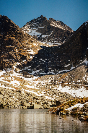 Popradske mountain lake and snowy High Tatras in the background on a sunny day in Slovakia. Shot with film camera and grainの写真素材